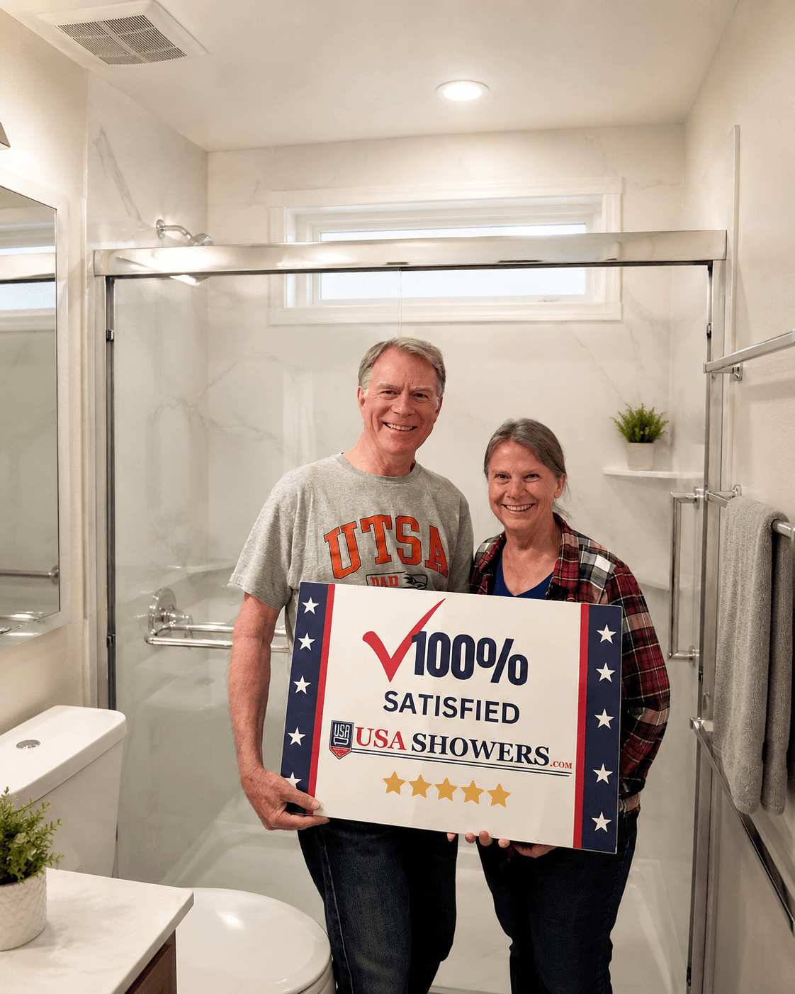 Happy customers holding 100% satisfied sign from USA Showers in front of their new shower remodel